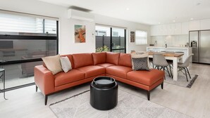 A modern living room with a sectional sofa, a dining area, and a kitchen.