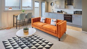 Una sala moderna con un sofá, sillones, una mesa de centro y una cocina al fondo.