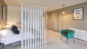 Un dormitorio con cama, un separador blanco, una silla verde, un radiador y un cuadro en la pared.