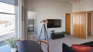 A modern living room with a dining table, chairs, a sofa, a television, and a tripod. - Host & Stay | Skipper's Rest @ North Marine House (Scarborough)