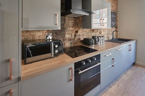 Une cuisine moderne dotée d’une cuisinière, d’un four et d’un micro-ondes encastrés, d’un plan de travail en granit et d’un mur de fond en briques apparentes.