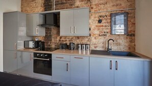 A modern kitchen with grey cabinets, a brick wall, and a black sink. - Host & Stay | Skipper's Rest @ North Marine House (Scarborough)