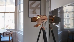A room with a tripod-mounted camera on a tripod, a framed abstract artwork on the wall, and a window with a view of buildings. - Host & Stay | Skipper's Rest @ North Marine House (Scarborough)