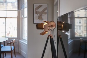 Une pièce dans laquelle on trouve un appareil photo fixé sur un trépied, une œuvre d’art abstraite encadrée accrochée au mur et une fenêtre donnant sur des immeubles.