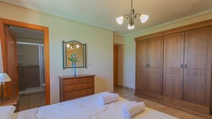A bedroom with a large bed, wooden wardrobe, and a mirror with a vase. - 016 - Finca La Dama Valverde - comfortHOLIDAYS (Valverde)