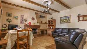 A cozy living room with a fireplace, leather sofa, dining table, and wooden beams on the ceiling. - 016 - Finca La Dama Valverde - comfortHOLIDAYS (Valverde)