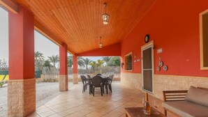 A covered patio with a wooden ceiling, a dining table with chairs, a sofa, and a bottle of wine. - 016 - Finca La Dama Valverde - comfortHOLIDAYS (Valverde)