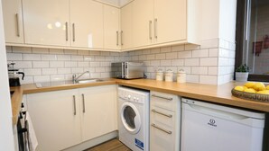 Una cocina moderna con armarios blancos, lavadora integrada y cafetera.
