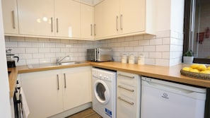 A modern kitchen with white cabinets, a built-in washing machine, and a coffee maker.