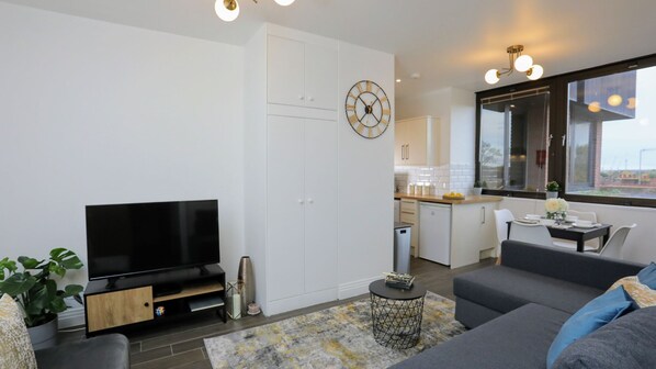 A modern living room with a flat-screen TV, a sofa, a coffee table, and a dining area with a table and chairs.