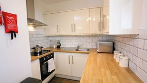 Una cocina compacta con armarios blancos, una campana extractora de acero inoxidable, horno empotrado, un lavabo y un tostador.