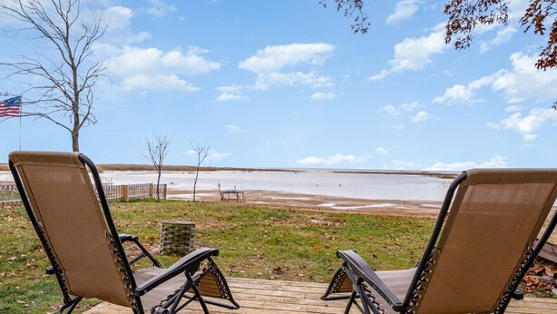 Two lounge chairs on a wooden deck overlooking a lake with a distant shoreline. - Cozy Home on Lake Huron I (Au Gres)