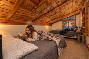 A cozy attic bedroom with a sloped ceiling, two beds, and a window with a view.