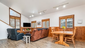 A cozy living area with a sofa, chairs, a dining table, and a TV. - Cozy Home on Lake Huron I (Au Gres)