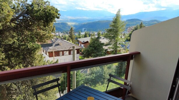 A balcony with a table and chairs, overlooking a scenic view of houses and mountains. - T2 Duplex with view, Garage, Balcony, Wifi (Font-Romeu-Odeillo-Via)
