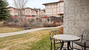 Un patio con una mesa y sillas de metal, un camino y un edificio con techo rojo al fondo.