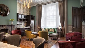 A spacious living room with a fireplace, green walls, and a large window with curtains. There are multiple seating areas with armchairs and a sofa. - Hapimag Apartments London (London)