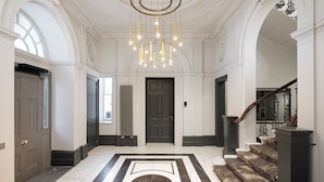 A grand foyer with a marble floor, a staircase, and a chandelier. - Hapimag Apartments London (London)
