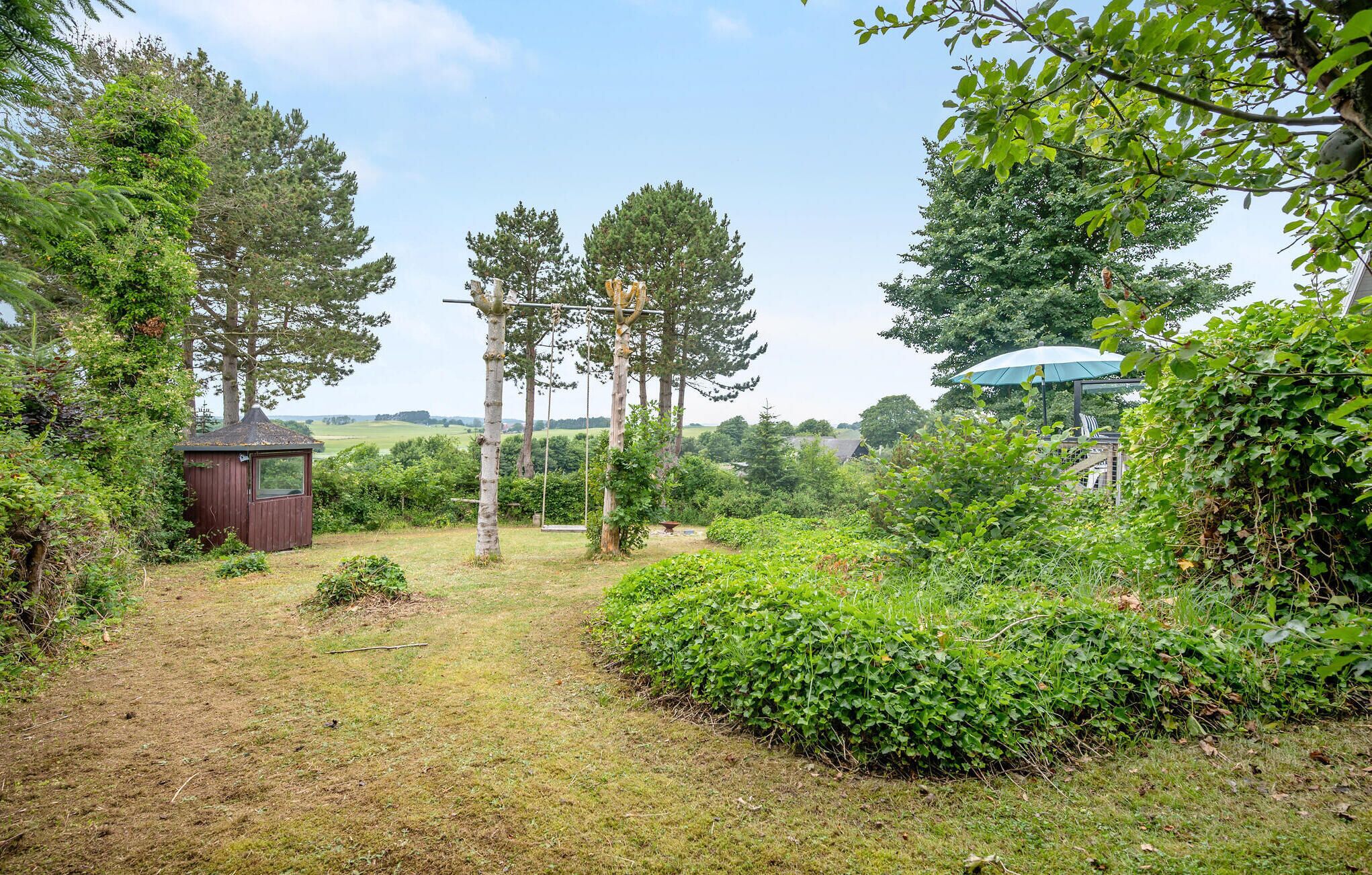 A garden with a wooden shed, a swing set, and a gazebo with a blue umbrella.