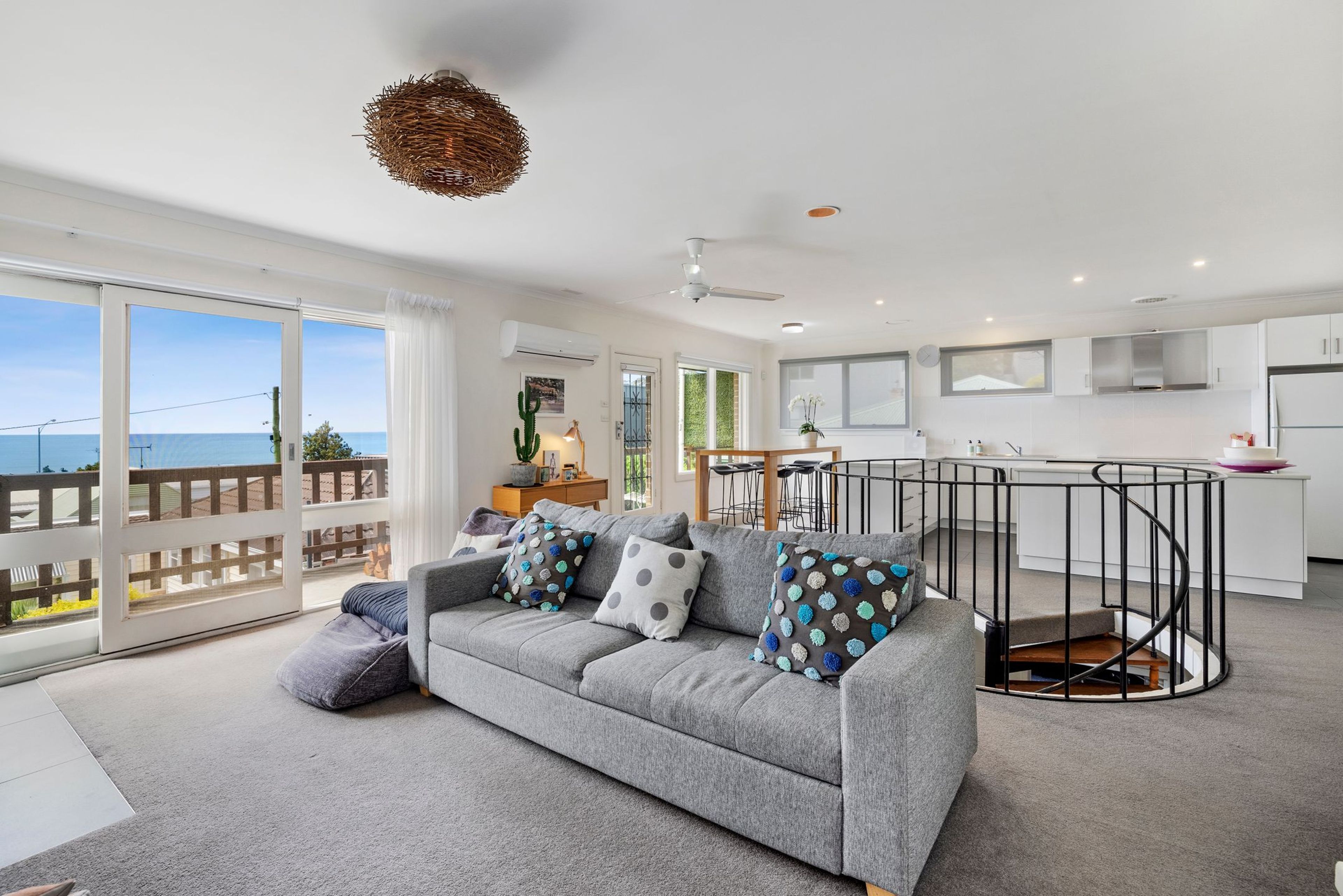 A modern living room with a grey sofa, a dining area with a round table, and a kitchen with white cabinets.