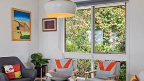 Relax in this serene living room with a garden view, featuring a comfortable sofa, a wooden chair, and modern decor.
