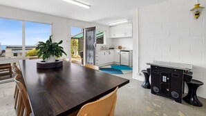 Una cucina moderna con mobili bianchi, un'area pranzo con tavolo e sedie in legno scuro e vista sull'oceano attraverso ampie finestre.