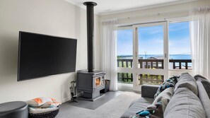 Relax in this stylish living room with a large flat-screen TV, wood-burning stove, and sliding glass door to a balcony with a sea view.