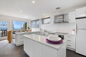 A modern kitchen with white cabinetry, a central island, and a view of the sea through large windows. - 1 Luana (Lorne)