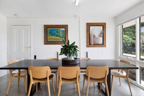 A dining area with a long table, six chairs, two framed artworks, and a potted plant. - 1 Luana (Lorne)