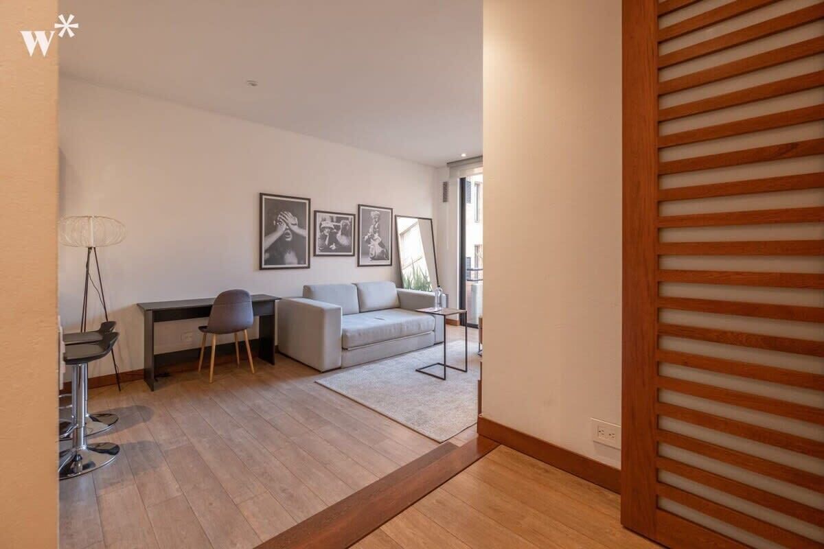 Una sala de estar moderna con un sofá, un escritorio y una silla. Hay cuadros enmarcados en la pared.