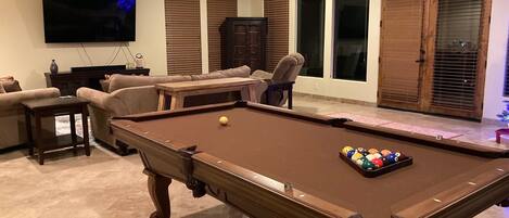 A living room with a pool table, a television, and a ceiling fan.