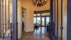 A spacious hallway with a curved ceiling and a chandelier, leading to a balcony with a view of the landscape.