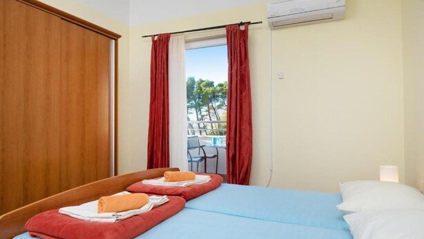 Hotelkamer met een bed, rode gordijnen, een raam met uitzicht op bomen en een airconditioning.