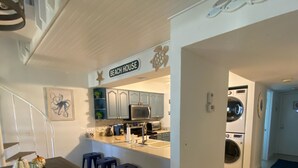 Een moderne keuken met een centraal eiland, barstoelen en een bord waarop 'Beach House' staat.