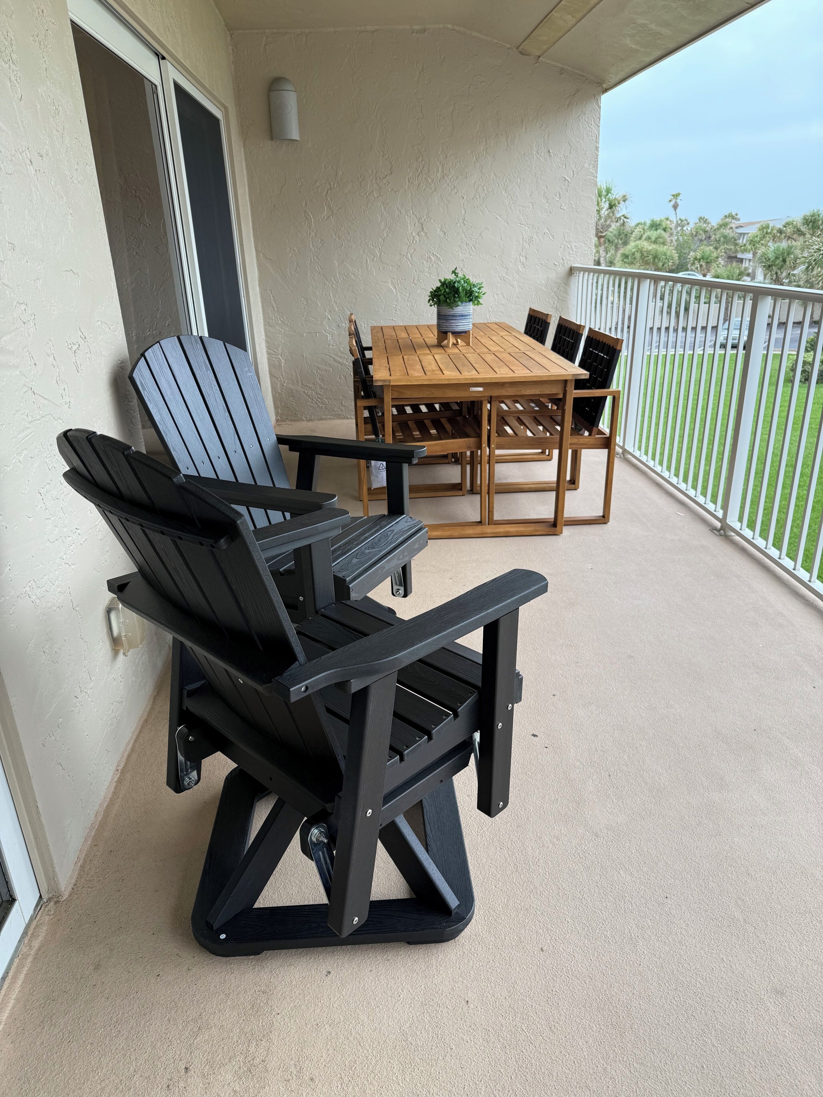 A balcony with a wooden table and chairs, a potted plant, and a view of the surrounding area.