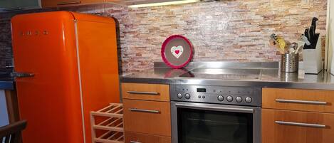 A kitchen with a wooden cabinet, an oven, a stainless steel countertop, and a red refrigerator.