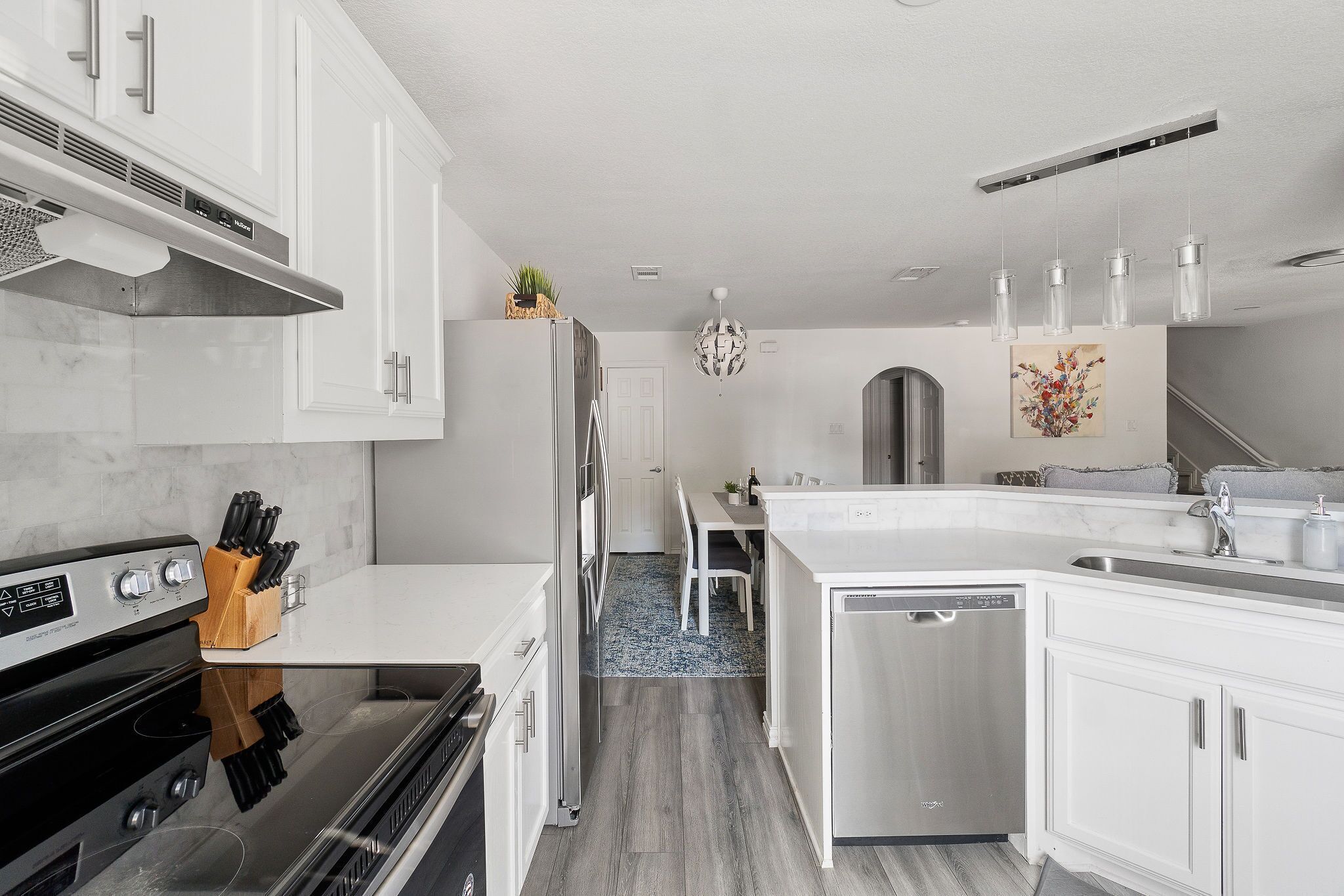 A modern kitchen with white cabinetry, a stainless steel refrigerator, a built-in oven, and a dishwasher.