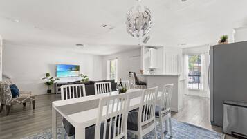 A modern living room with a dining area, a kitchen, and a TV displaying a scenic view.