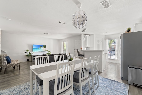 A modern living room with a dining area, a kitchen, and a TV displaying a scenic view.