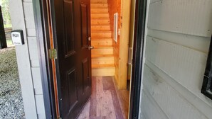 A wooden exterior with a black door, a visible staircase inside, and a 'hello' mat at the entrance.
