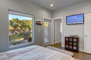 A bedroom with a large window, a bed, a TV, and a small cabinet. - A Pet Friendly Tropical Oasis! (Port Aransas)