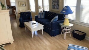 A living room with a blue sofa, white coffee table, and a lamp on a side table. - Peace and quiet within short walking distance to the beach.  (Ocean City)