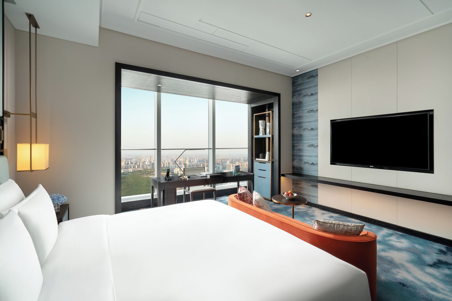 A modern hotel room with a large bed, a desk with a view, a flat-screen TV, and a cityscape view.