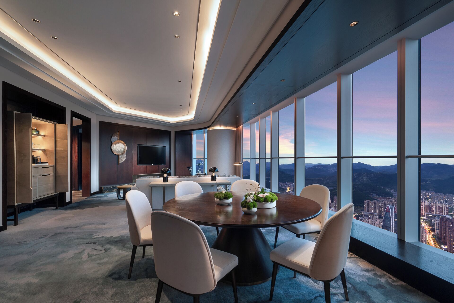 Un comedor moderno con vistas panorámicas a la ciudad, una gran mesa redonda y sillas contemporáneas.