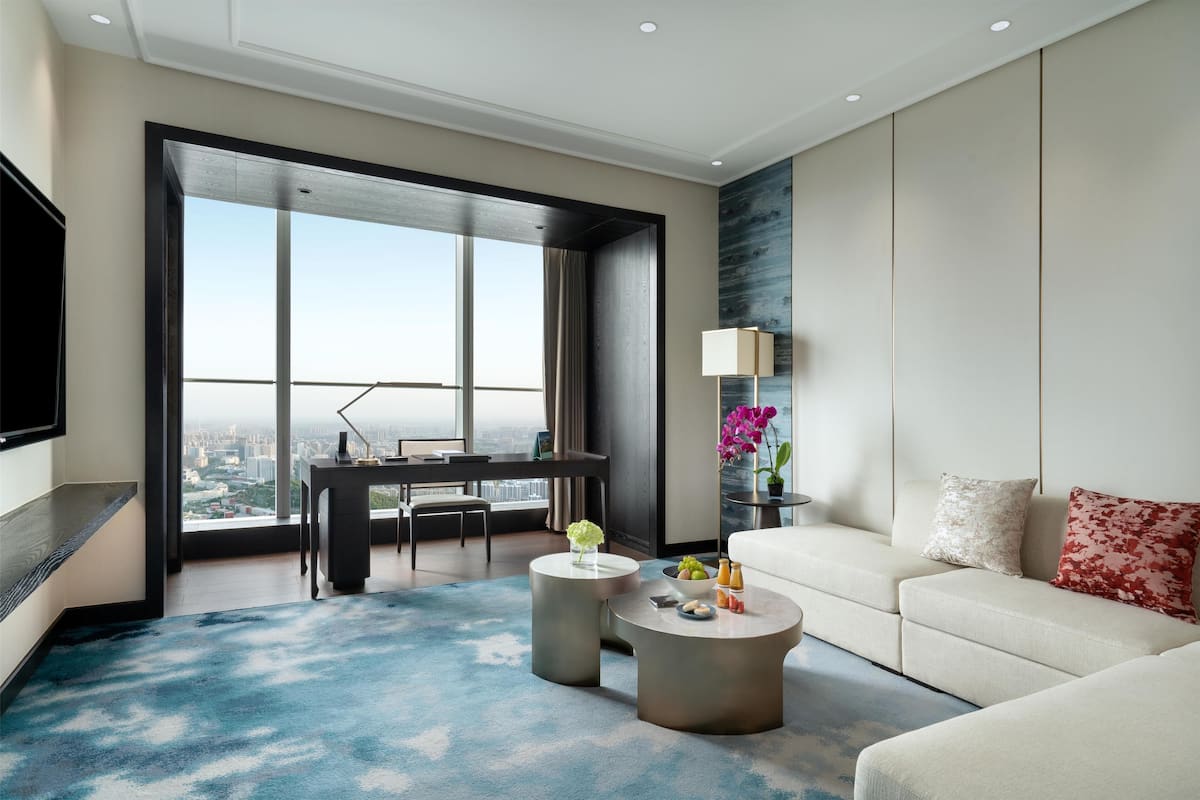 Une chambre d’hôtel moderne dotée d’une grande fenêtre, d’un téléviseur à écran plat, d’un canapé, d’une table basse et d’un bureau avec une chaise.