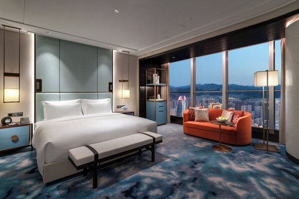 Habitación de hotel moderna con una cama grande, un banco, un sofá y vistas a un paisaje urbano a través de amplios ventanales.