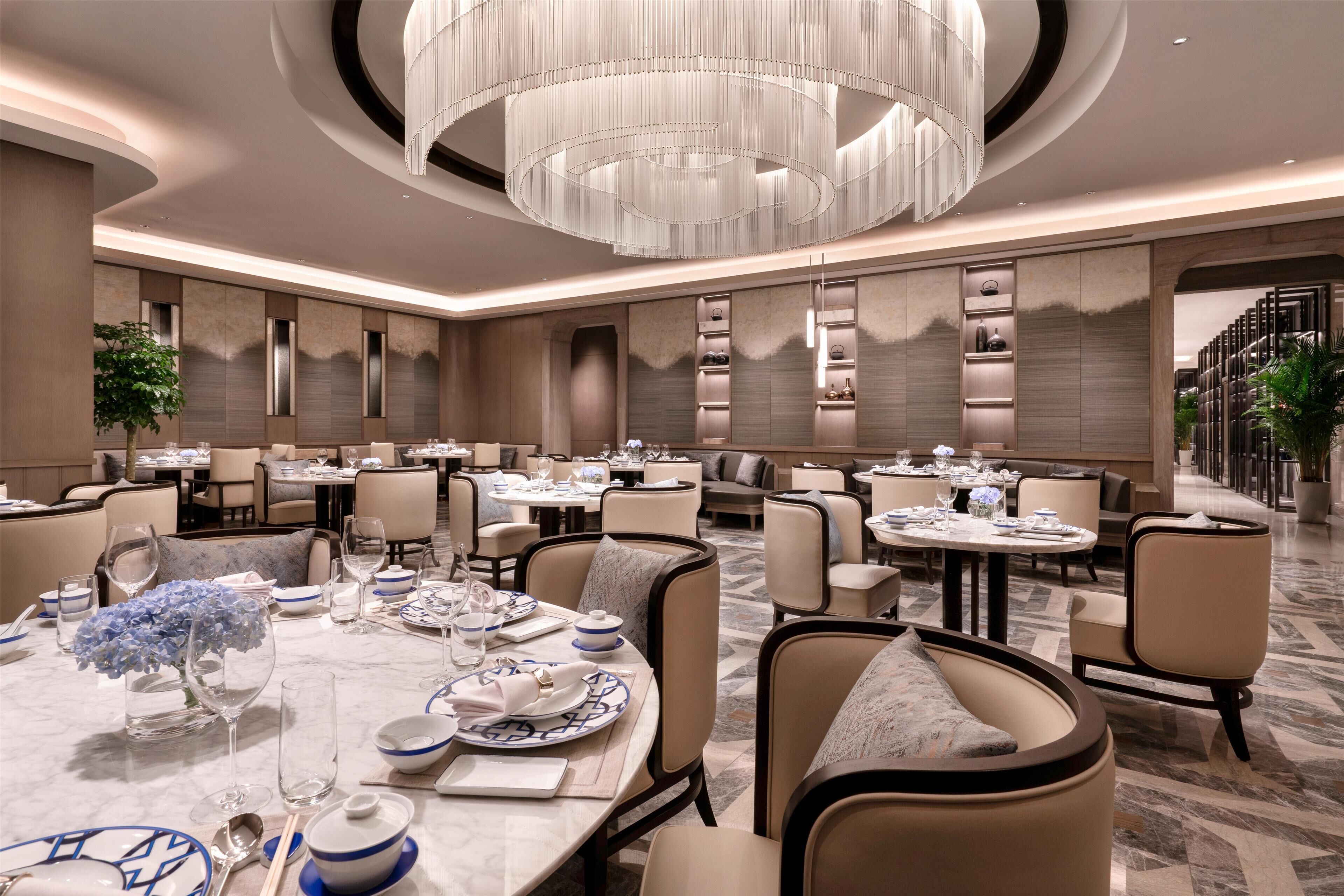 A spacious dining area with multiple tables set for dining, elegant chandeliers, and a modern interior design.