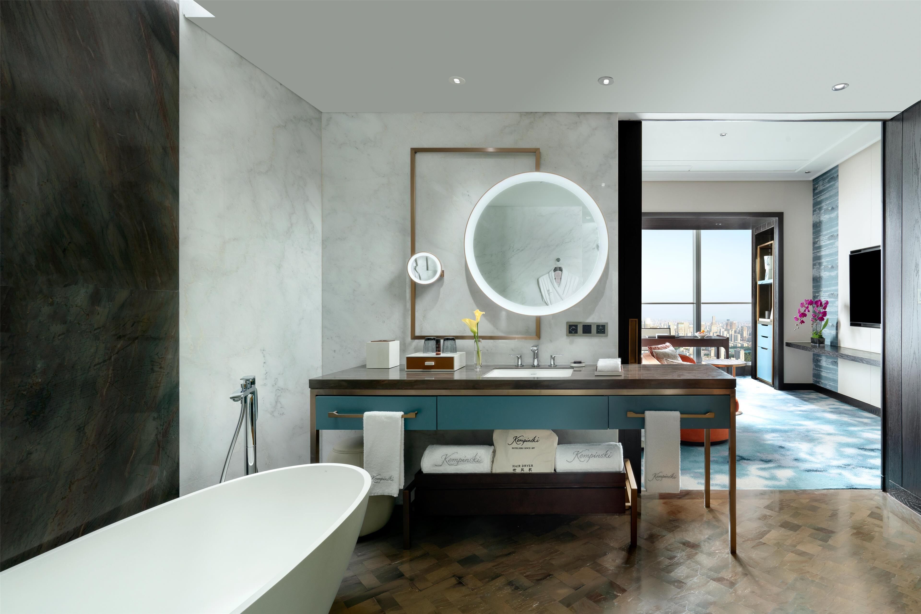 A modern bathroom with a large bathtub, a round mirror, and a vanity with a sink.
