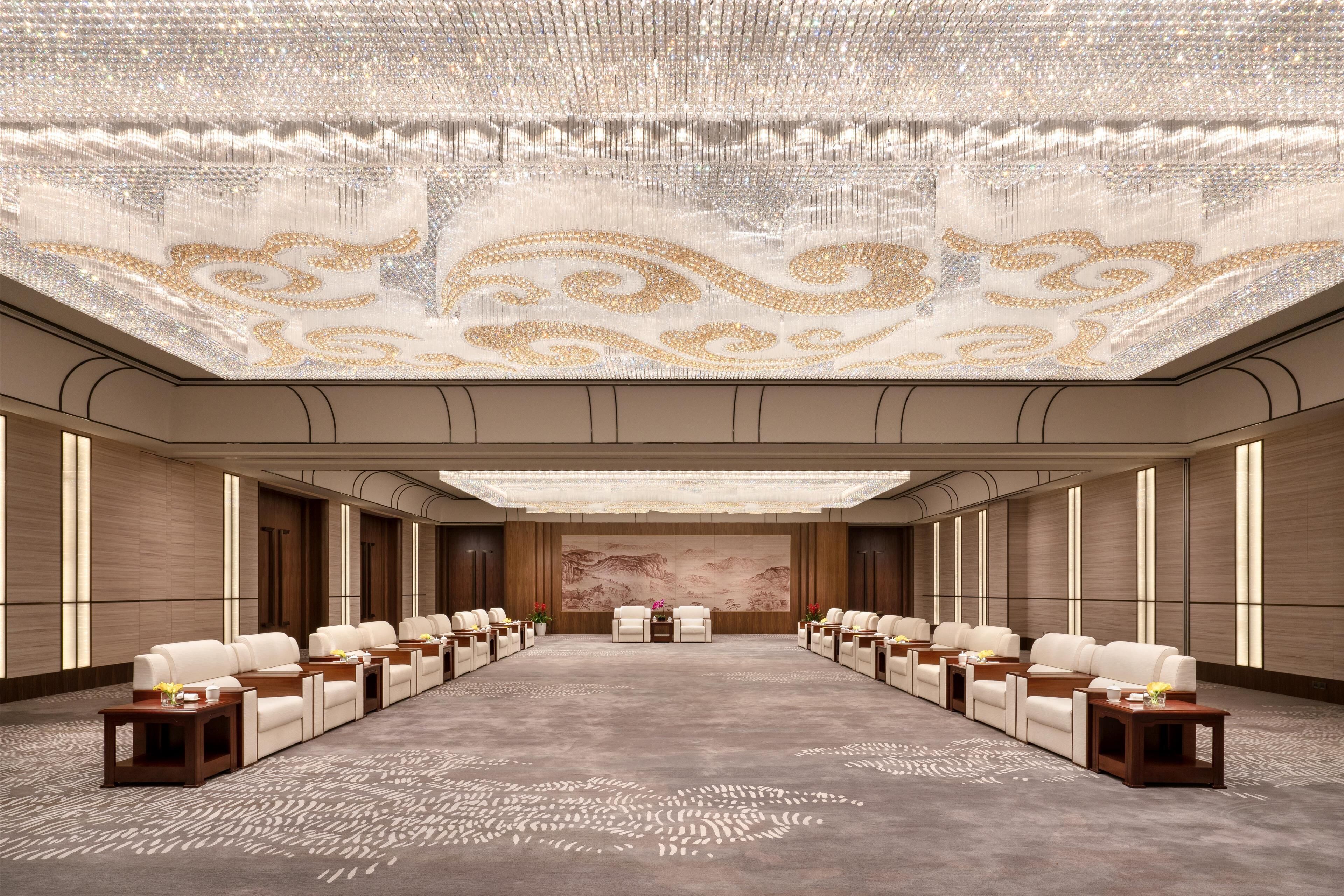 A conference room with a long table, rows of chairs, and a large chandelier.