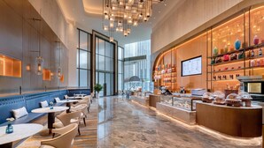 Un hall d’hôtel moderne doté d’un espace salon, d’un présentoir de nourriture et d’une grande fenêtre laissant entrer la lumière naturelle.